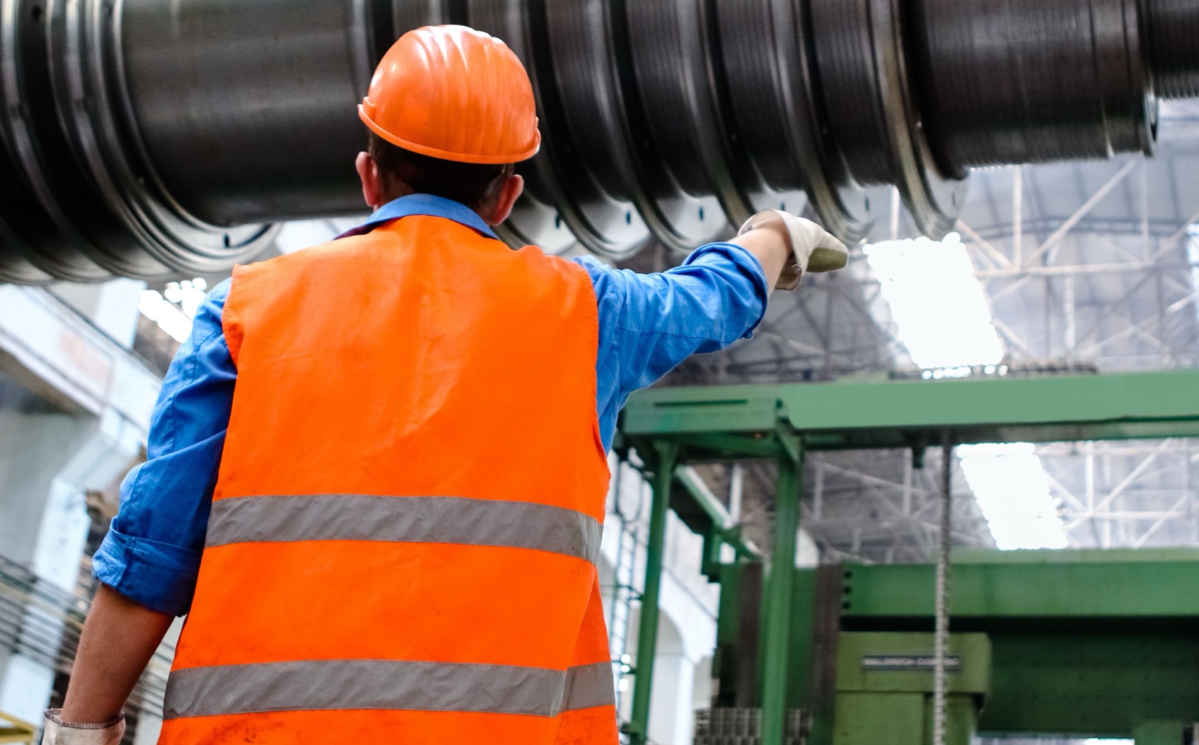 Worker in an orange high-visibility vest with two silver retroreflective bands, on a factory floor