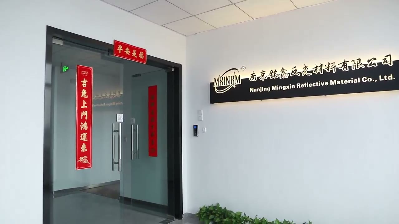 Still from factory video: office entrance with the illuminated company signboard reading Nanjing Mingxin Reflective Material Co., Ltd.